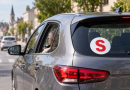 Voiture grise circulant en ville avec un macaron S rouge apposé à l’arrière, illustrant l’autocollant utilisé par certains conducteurs seniors en France.
