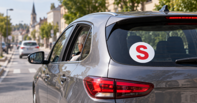Voiture grise circulant en ville avec un macaron S rouge apposé à l’arrière, illustrant l’autocollant utilisé par certains conducteurs seniors en France.