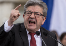 Jean-Luc Mélenchon, fondateur de La France insoumise (LFI), photographié dans une attitude très véhémente lors d’une prise de parole politique, le visage tendu, la bouche ouverte et l’index levé devant des micros, avec les couleurs du drapeau français en arrière-plan.