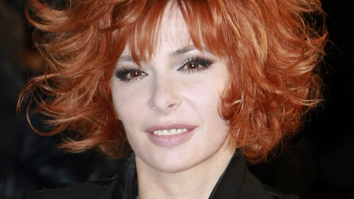 Portrait rapproché de Mylène Farmer, avec sa chevelure rousse emblématique et une tenue noire.